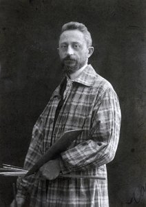 Retrato de três quartos do pintor Guido Spadolini. Ele está vestindo uma blusa longa e segurando pincéis e paleta em sua mão esquerda, 26111901