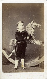 Menino de pé ao lado de um cavalo de balanço de Silas Eastham