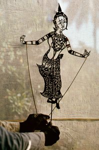 O marionetista manipula uma marioneta de sombras para contar histórias contra uma tela para um jogo de sombras. C...