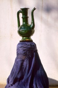 Uma mulher em Cabul, isolada do olhar por um chador de seda, transporta um jarro de uma...