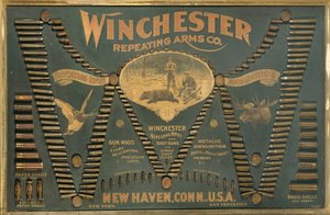 Uma placa de exibição do cartucho Winchester, com uma seleção abrangente de cartuchos de espingarda e cartuchos metálicos, de latão e de papel, dispostos na forma de um "W" estendido de Unbekannt