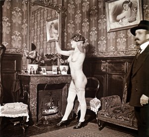 Fotografia enigmática que mostra uma jovem mulher completamente nua (exceto os sapatos e as meias) a pentear-se em frente a um espelho na presença de um homem vestido e aquecido com um chapéu. Poder-se-ia pensar que se tratava de uma fotografia tirada num  de Unbekannter Künstler