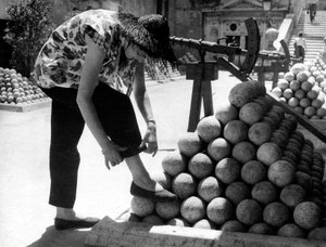 Uma mulher ajusta o punho das calças enquanto apoia o pé numa pilha de balas de canhão no recinto do Castelo de Santo Ângelo, em Roma. de Unknown photographer