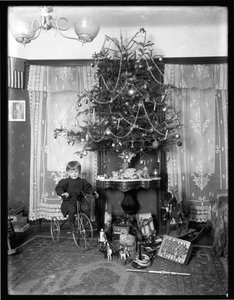 Seymour menino posou sentado no triciclo ao lado da árvore de Natal na sala de estar, Natal de 1912 de William Davis Hassler