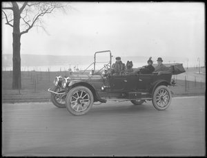 Três pessoas não identificadas e dois cães Chow dirigindo em um carro conversível ao longo de um rio ou lago, c.1912 de William Davis Hassler