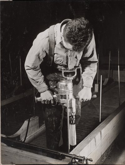 [Um homem utiliza uma máquina manual para trabalhar com um pedaço de madeira]. de Arnold Eagle