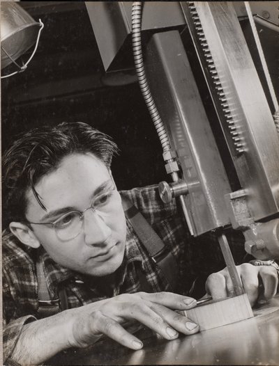 [Homem de óculos trabalha atentamente com um ficheiro industrial] de Arnold Eagle
