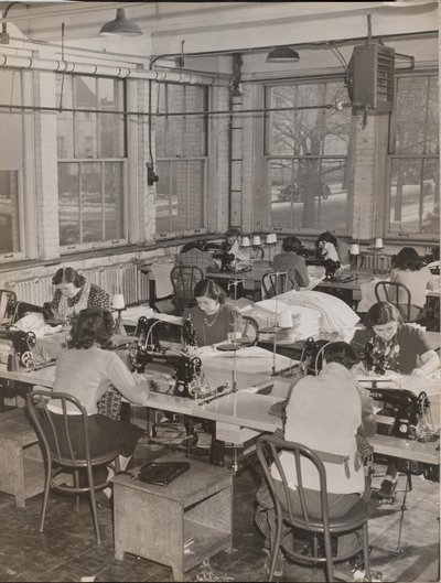 [Mulheres sentadas em secretárias trabalham em máquinas de costura]. de Arnold Eagle