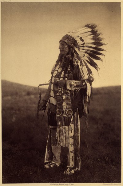 Gavião-alto. Vestidos de guerreiro para uma grande ocasião: camisa de couro, leggings, mocassins, bainha de cachimbo (todos bordados com piques de porco-epic), touca de guerra com penas de águia, bastão com cabeça de pedra, com um couro cabeludo. Exercício de Edward Sheriff Curtis