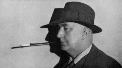 Retrato de Edgar Wallace, de chapéu e a fumar um cigarro numa pega (fotografia a preto e branco) de English Photographer