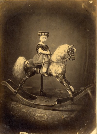 Jovem rapariga sentada num cavalo de baloiço de English Photographer