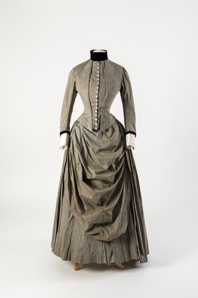 Vestido de algodão cinzento com avental drapeado na frente e corte de veludo preto no colarinho e punhos, final da década de 1880 (algodão) de English School