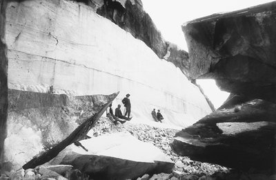 Alguns homens sentados ao longo das paredes de uma pedreira de mármore, nos Alpes Apuanos (foto a p/b) de G. Armani