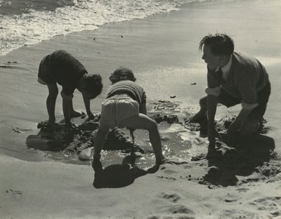 Três crianças a brincar com areia na praia. de Godfrey Macdominic