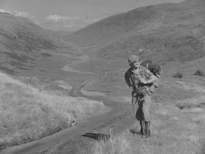 Um homem a caminhar com uma mochila às costas numa paisagem de vale aberto de Joseph Hardman