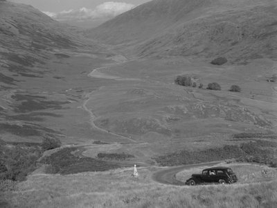 Uma mulher de pé com vista para um vale aberto, com um carro estacionado nas proximidades de Joseph Hardman