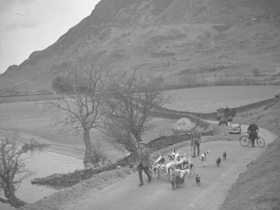 Dois homens a passear com cães de caça numa estrada, atrás um homem com uma bicicleta e maquinaria, palheiro e lago à esquerda da imagem, montanhas ao fundo de Joseph Hardman
