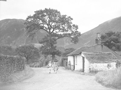 Duas jovens de mãos dadas, segurando ramos de dedaleiras, a caminhar pela estrada, passando pela casa de campo em direção à câmara de Joseph Hardman