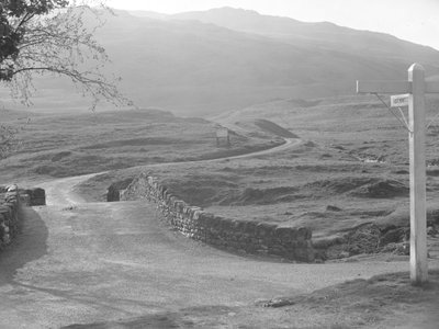 Vista da estrada que passa sobre Hardknott Pass com um sinal a apontar na direção de Hardknott de Joseph Hardman