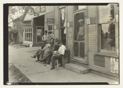Homens com cão sentados num banco em frente a um armazém geral de Lewis Wickes Hine