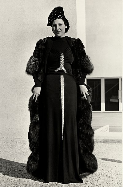 Modelo em vestido de noite criado pela casa de alta costura italiana "Dragoni". A fonte do artigo tem uma decoração de lantejoulas brilhantes em forma de espada. Um chapéu e um sobretudo de pele completam o conjunto. (foto a p/b) de Luis Bogino