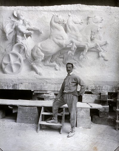 Retrato em tamanho real do famoso escultor Pietro Canonica. Ele está posando em seu estúdio diante de um alto relevo de mármore em que ele está trabalhando (foto a p/b) de Mario Nunes Vais