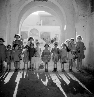 Crianças europeias em uniforme escolar sob um arco com sombras. de Maynard Owen Williams