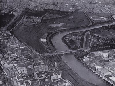 Melbourne: Uma vista aérea dos Jolimont Railway Yards e do Rio Yarra, mostrando um pequeno trecho da cidade e Richmond à distância (foto a p/b) de Photographer Australian