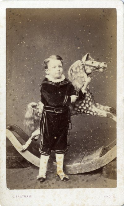 Menino de pé ao lado de um cavalo de balanço de Silas Eastham