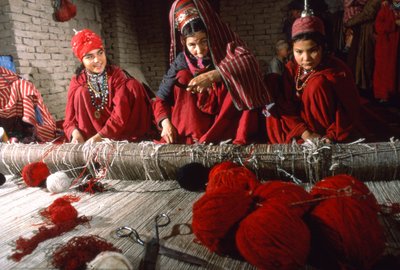 Mulheres de tribos turcomanas tecelãs cortam os nós da urdidura de um tapete num tear na aldeia de... de Thomas J. Abercrombie