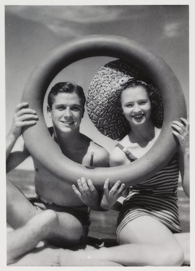 Homem e mulher olhando através de um anel de borracha na praia, c 1935 de Unbekannt