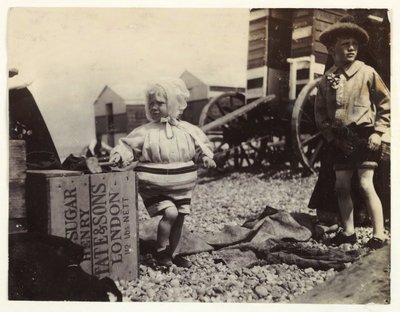 Duas crianças por máquinas de banho, c 1895, Uma fotografia de duas crianças à beira-mar, em pé no meio de um grupo de máquinas de banho na praia de Unbekannt