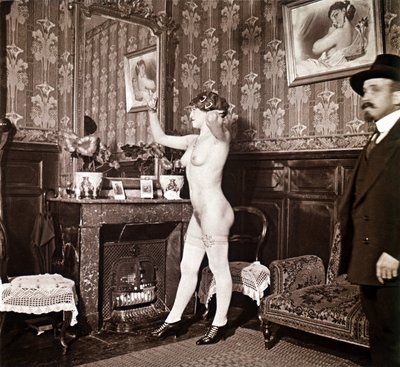 Fotografia enigmática que mostra uma jovem mulher completamente nua (exceto os sapatos e as meias) a pentear-se em frente a um espelho na presença de um homem vestido e aquecido com um chapéu. Poder-se-ia pensar que se tratava de uma fotografia tirada num  de Unbekannter Künstler