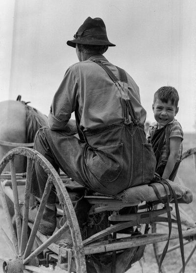 Agricultor e rapaz sorridente andam no assento de uma charrete puxada por cavalos na Virgínia Ocidental de Volkmar Wentzel