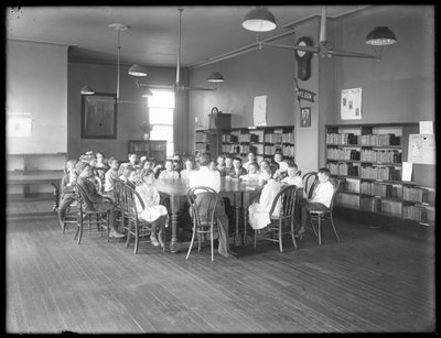 Crianças ouvem uma mulher na sala de leitura de um ramo não identificado da Biblioteca Pública de Queens Borough, c.1910 de William Davis Hassler