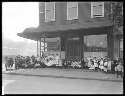 As crianças posam em frente a uma filial de loja não identificada da Biblioteca Pública Queens Borough, Nova York, c.1910 de William Davis Hassler