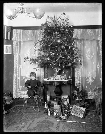 Seymour menino posou sentado no triciclo ao lado da árvore de Natal na sala de estar, Natal de 1912 de William Davis Hassler