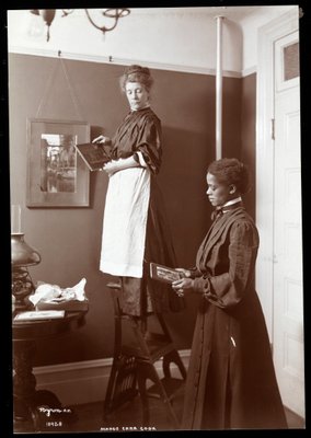 Madge Carr Cook pendurar fotos com sua empregada, c.1904 (impressão de gelatina de prata) de Byron Company