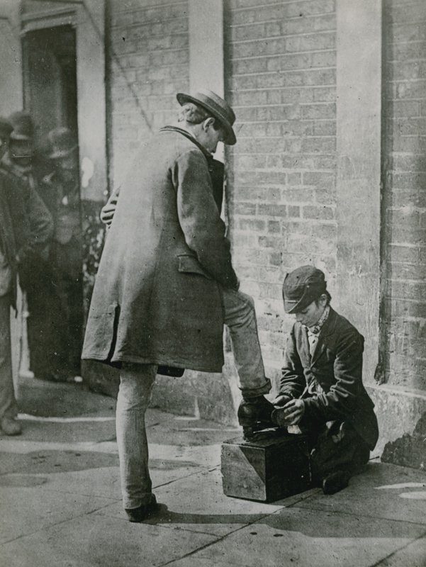 Um jovem shoeblack brilhando um homem sapatos na rua de English Photographer