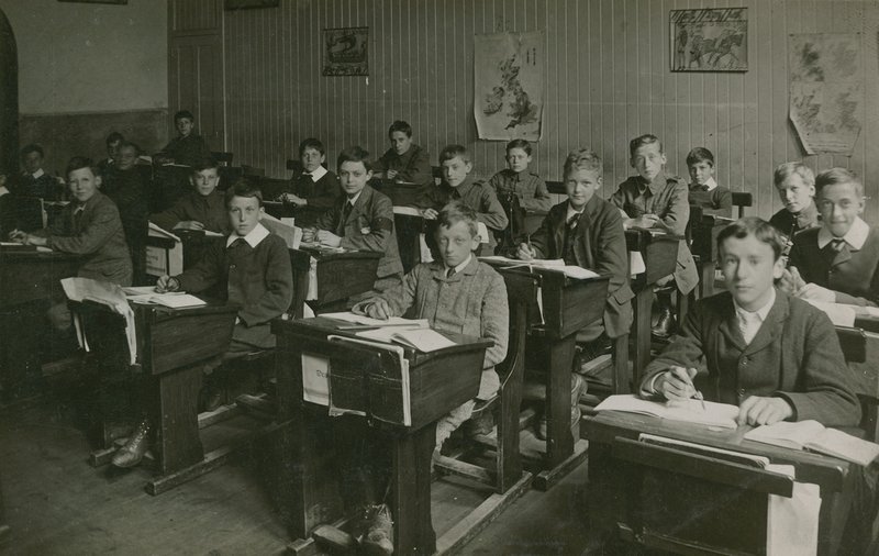 Alunos masculinos sentado atrás de suas mesas durante uma aula na escola de English Photographer