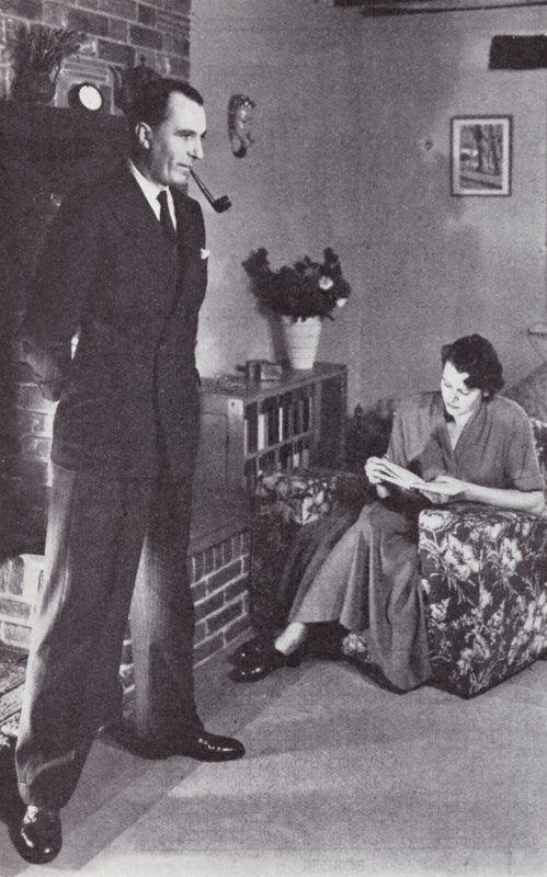 A esposa lê, enquanto o marido aquece as costas contra o fogo, c.1950 de English Photographer
