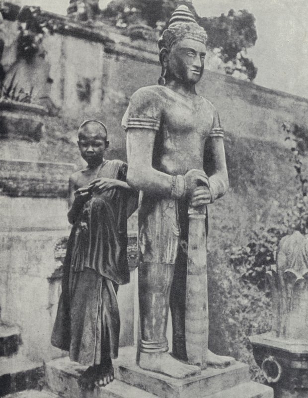 Jovem monge budista noviço ao lado de uma estátua de Buda, Indochina Francesa (foto a p/b) de Ewing Galloway