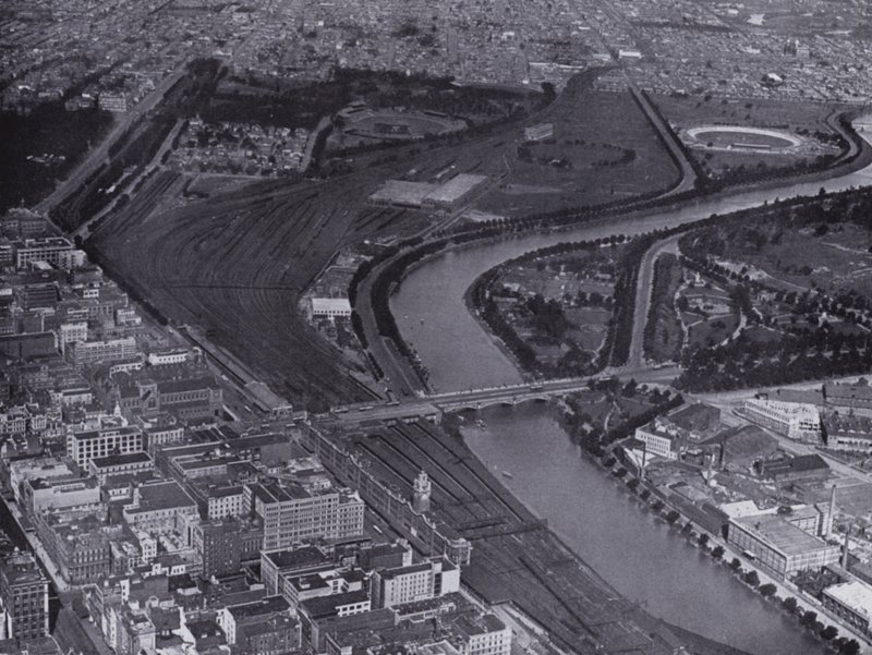 Melbourne: Uma vista aérea dos Jolimont Railway Yards e do Rio Yarra, mostrando um pequeno trecho da cidade e Richmond à distância (foto a p/b) de Photographer Australian