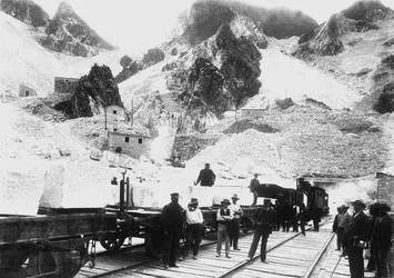 Escavadoras em frente de um comboio ferroviário carregado com blocos de mármore em Ravaccione, nos Alpes Apuanos (foto a p/b)