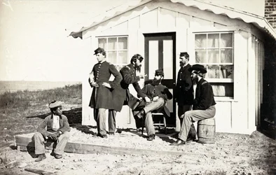Cinco soldados da Guerra Civil se reuniram na varanda suja fora de casa, juventude afro-americana sentada perto deles, 1861-65