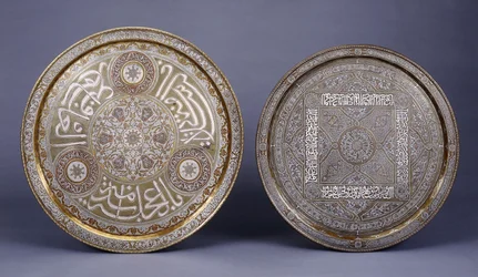 Duas bandejas circulares de latão incrustadas em ouro, cobre e prata, decoradas com arabescos e inscrições, finais do século XIX