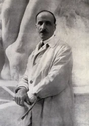 Retrato de três quartos do escultor Edoardo Rubino com martelina na mão. No fundo, um esboço pode ser feito