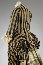 Vestido de noite, c.1884 (vista parcial oblíqua das costas). Cetina de seda e veludo cortado, renda, borlas de fio de seda e franja. Charles Frederick Worth, França.