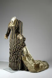 Vestido de noite, c.1884 (vista lateral oblíqua). Cetina de seda e veludo cortado, renda, borlas de fio de seda e franja. Charles Frederick Worth, França.
