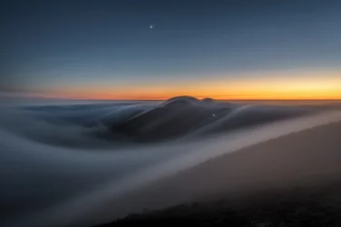 Montanhas ao crepúsculo acima das nuvens